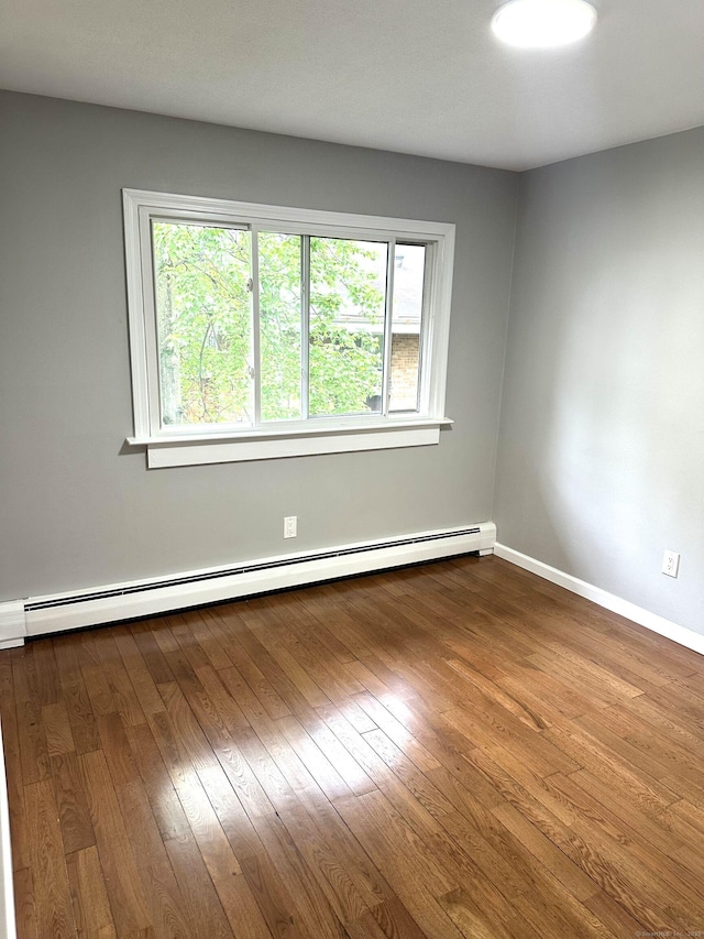 spare room featuring a baseboard heating unit, baseboards, and dark wood-style flooring