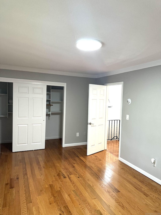 unfurnished bedroom featuring crown molding, wood finished floors, a closet, and baseboards