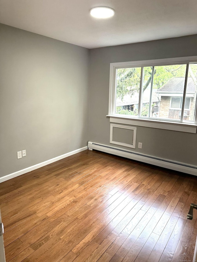 unfurnished room featuring a baseboard radiator, healthy amount of natural light, wood-type flooring, and baseboards
