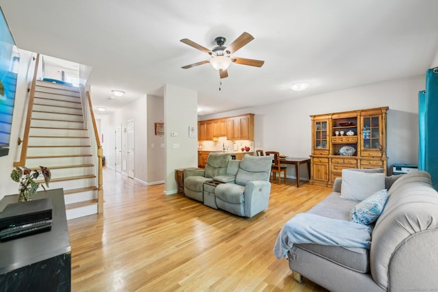 living area with stairway, light wood-style flooring, ceiling fan, and baseboards