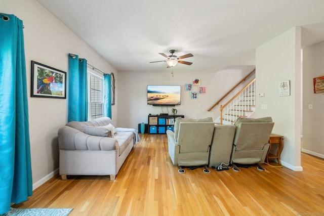 living area with light wood-style floors, ceiling fan, baseboards, and stairway