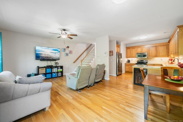 living room with light wood-style floors, stairway, a ceiling fan, and baseboards