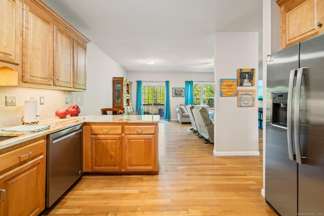 kitchen featuring appliances with stainless steel finishes, a peninsula, light wood finished floors, and light countertops