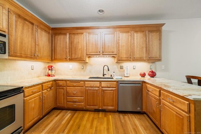 kitchen featuring appliances with stainless steel finishes, a sink, a peninsula, and brown cabinetry