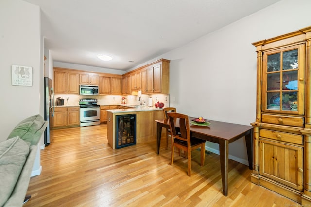 kitchen featuring stainless steel appliances, a peninsula, open floor plan, light wood finished floors, and a sink