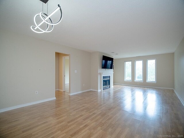 500 Prospect St Apt 3G, New Haven, CT 06511 - unfurnished living room featuring light wood-style flooring, a glass covered fireplace, baseboards, a chandelier, and a textured ceiling