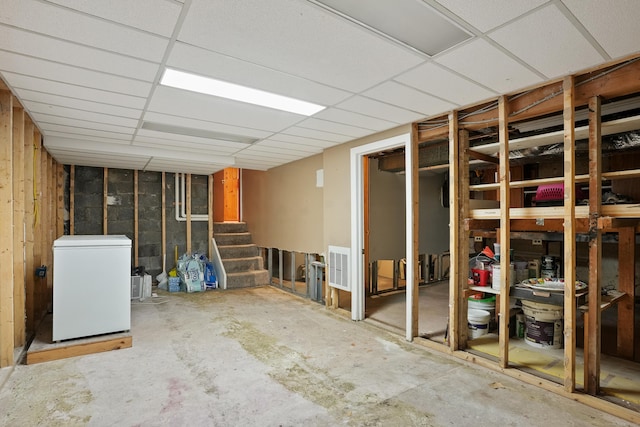 unfinished below grade area featuring fridge, stairs, and a drop ceiling