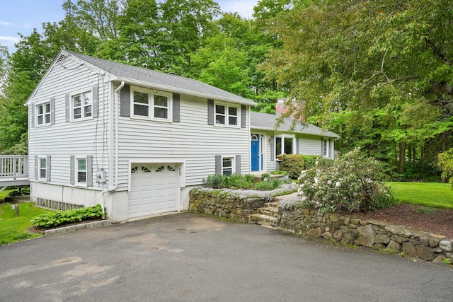 tri-level home with asphalt driveway, an attached garage, a chimney, and a shingled roof
