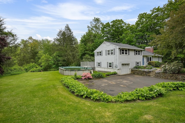 back of property with asphalt driveway, a garage, a chimney, a yard, and a deck