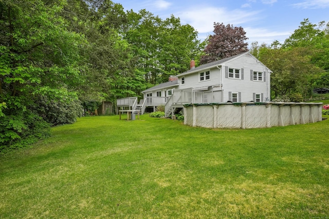 view of green lawn featuring a deck, a covered pool, stairway, and view of wooded area