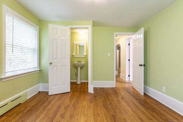 179 Parker Rd, Somers, CT 06071 - unfurnished bedroom featuring baseboard heating, arched walkways, wood finished floors, and baseboards