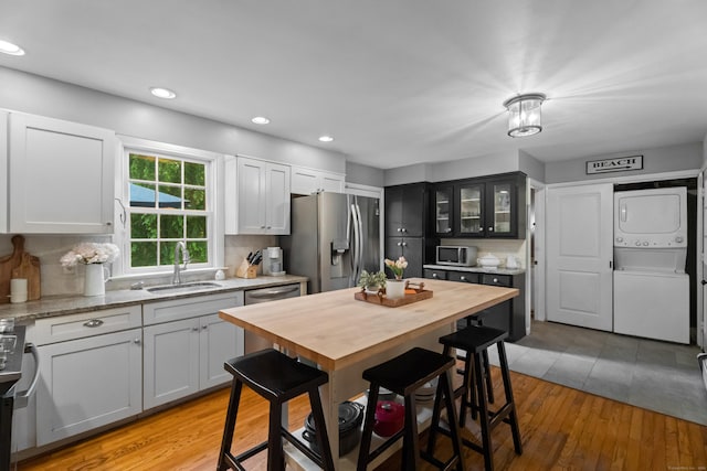 57 Elm Ridge Rd, Stonington, CT 06379 - kitchen with stacked washing machine and dryer, stainless steel refrigerator with ice dispenser, light wood-style floors, glass insert cabinets, and recessed lighting