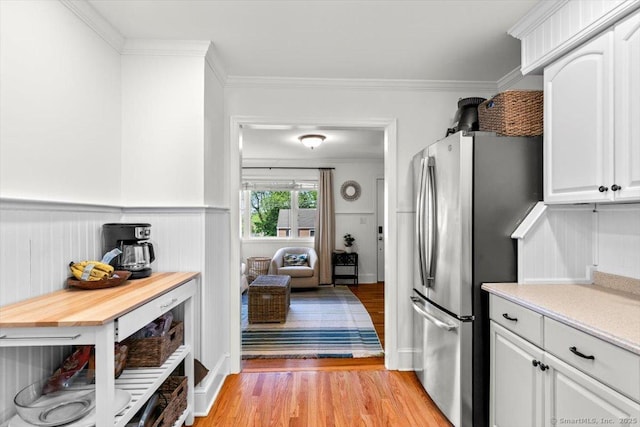 kitchen featuring freestanding refrigerator, light wood-style flooring, light countertops, white cabinetry, and crown molding