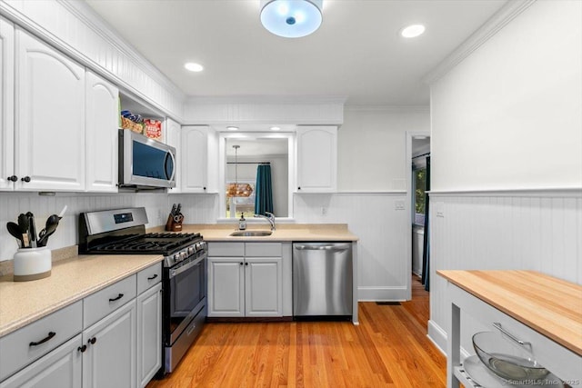 kitchen with appliances with stainless steel finishes, a sink, light countertops, light wood-type flooring, and a wainscoted wall