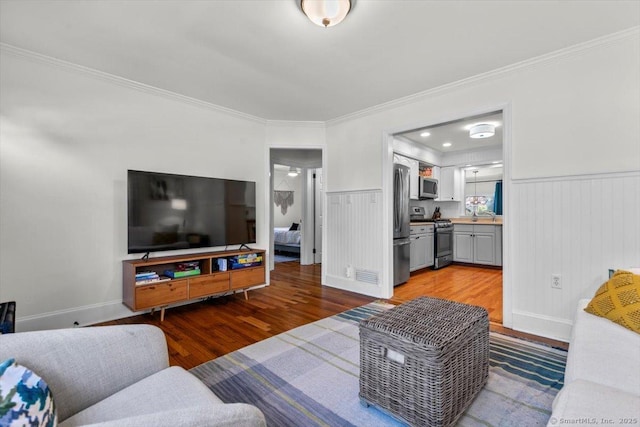 living room with wood finished floors, ornamental molding, and wainscoting