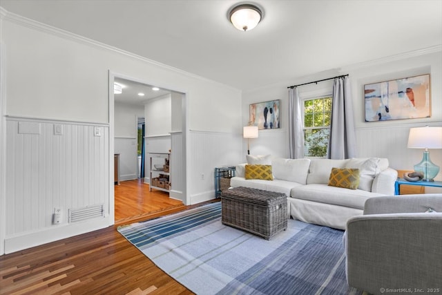 living area featuring crown molding, wood finished floors, a wainscoted wall, and a decorative wall
