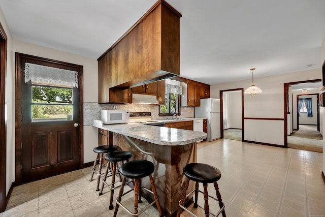 kitchen with white appliances, under cabinet range hood, healthy amount of natural light, and light countertops