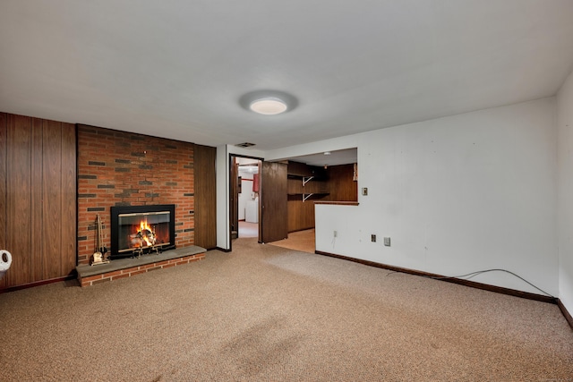 unfurnished living room with a fireplace, baseboards, light carpet, and wooden walls