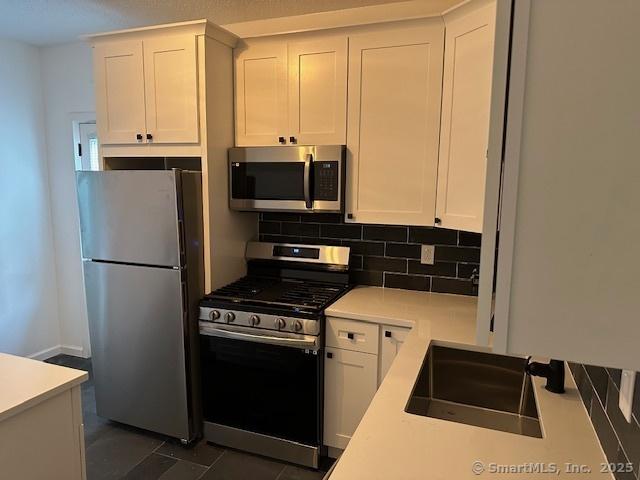 36 Bellevue Ave, Bristol, CT 06010 - kitchen with appliances with stainless steel finishes, a sink, white cabinets, and decorative backsplash