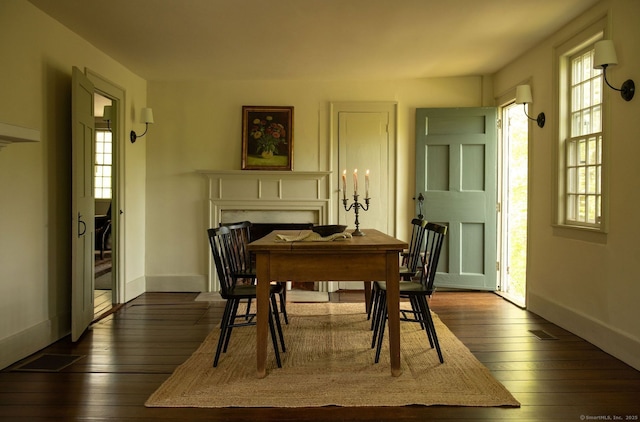 dining room featuring a fireplace, dark wood-type flooring, and baseboards
