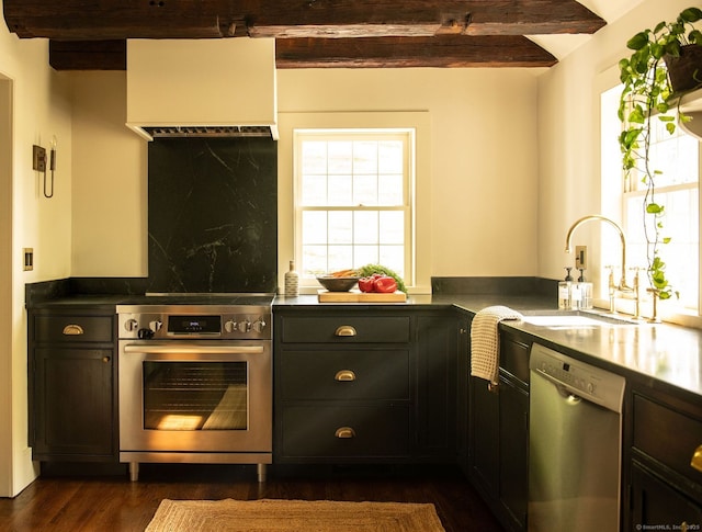 kitchen with stainless steel appliances, a sink, beamed ceiling, dark wood-style floors, and dark countertops