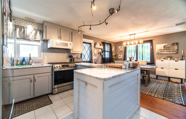 51 Palmetto Trl, East Haven, CT 06512 - kitchen featuring stainless steel gas range oven, white microwave, gray cabinets, decorative backsplash, and light tile patterned floors
