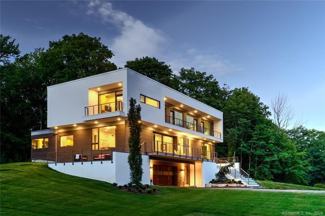 rear view of house with a balcony, stairway, a garage, a lawn, and stucco siding