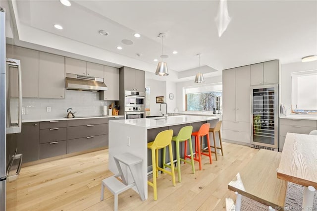 kitchen with gray cabinetry, wine cooler, under cabinet range hood, and recessed lighting