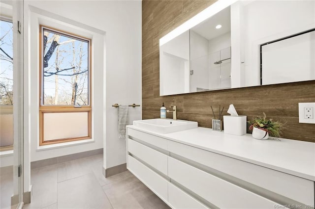bathroom with tile patterned floors, vanity, baseboards, decorative backsplash, and a shower
