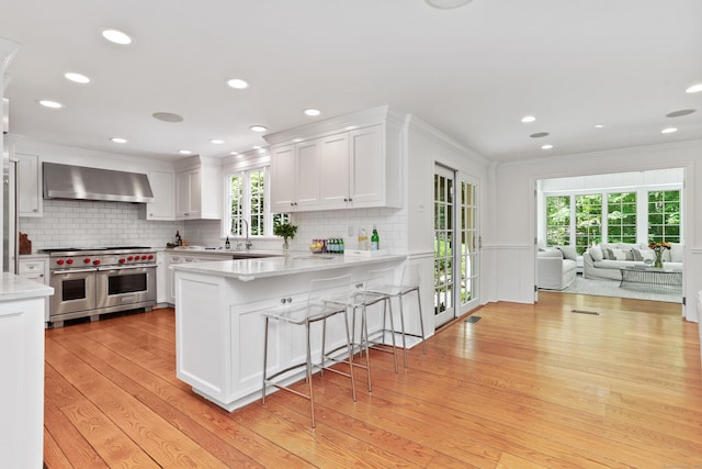 26 Heritage Ln, Weston, CT 06883 - kitchen featuring wall chimney range hood, double oven range, light wood-type flooring, white cabinets, and ornamental molding