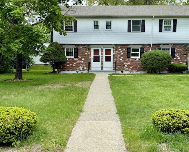 colonial house featuring brick siding, a front yard, and a shingled roof