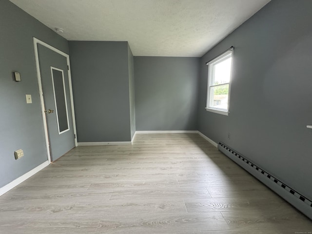 unfurnished room featuring a baseboard radiator, light wood finished floors, baseboards, and a textured ceiling