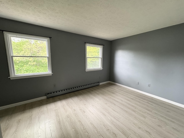 empty room with a baseboard heating unit, wood finished floors, a textured ceiling, and baseboards