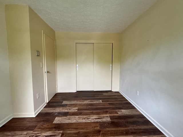 unfurnished bedroom featuring a textured ceiling, dark wood-style floors, baseboards, and a closet