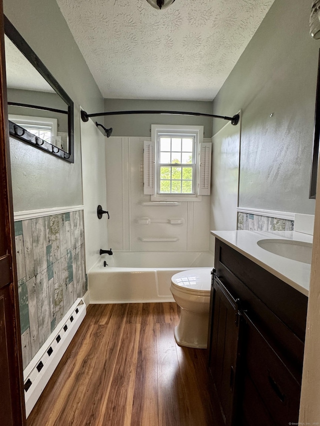 bathroom with a baseboard heating unit, wood finished floors, washtub / shower combination, vanity, and toilet