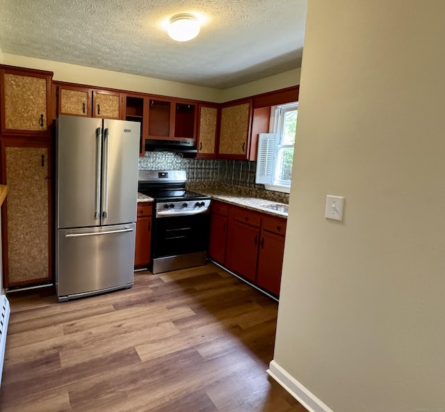 kitchen with appliances with stainless steel finishes, under cabinet range hood, light wood-type flooring, a textured ceiling, and open shelves