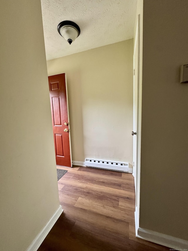corridor featuring baseboard heating, baseboards, wood finished floors, and a textured ceiling