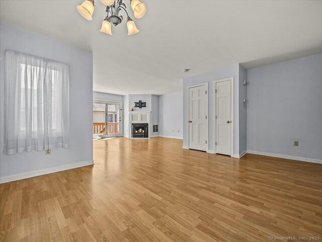 158 Paddock Ave Apt 2001, Meriden, CT 06450 - unfurnished living room featuring a chandelier, baseboards, light wood finished floors, and a lit fireplace