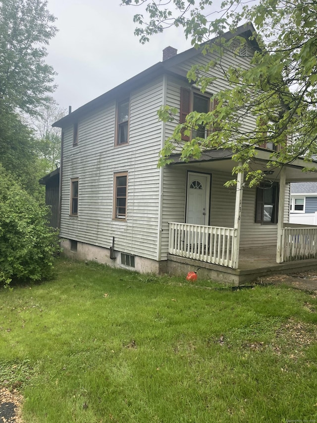 view of side of property featuring covered porch, a lawn, and a chimney