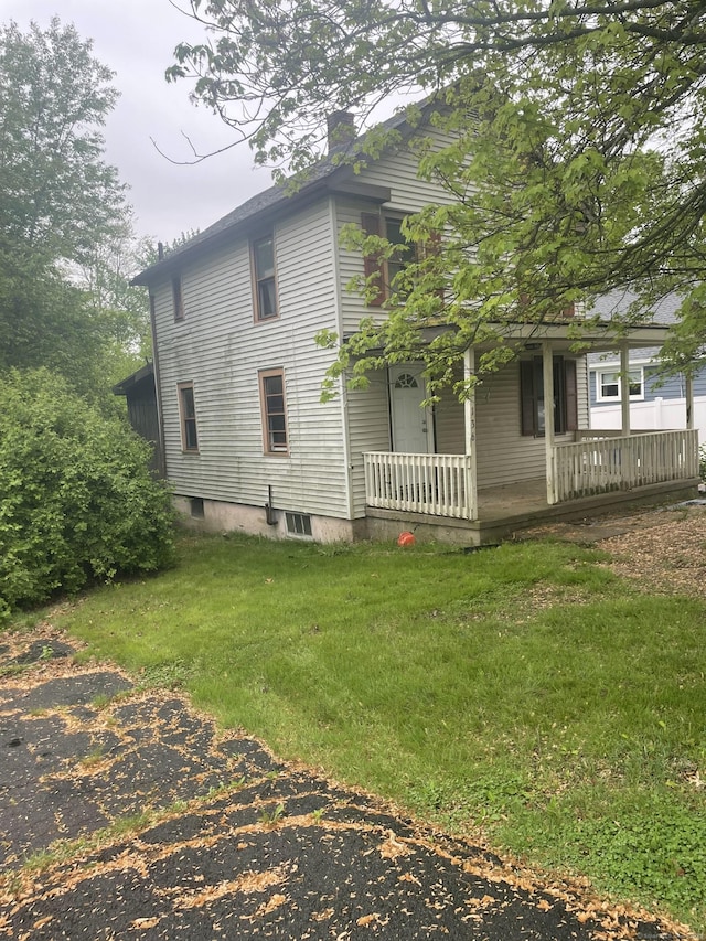 view of side of property featuring covered porch, a lawn, and a chimney