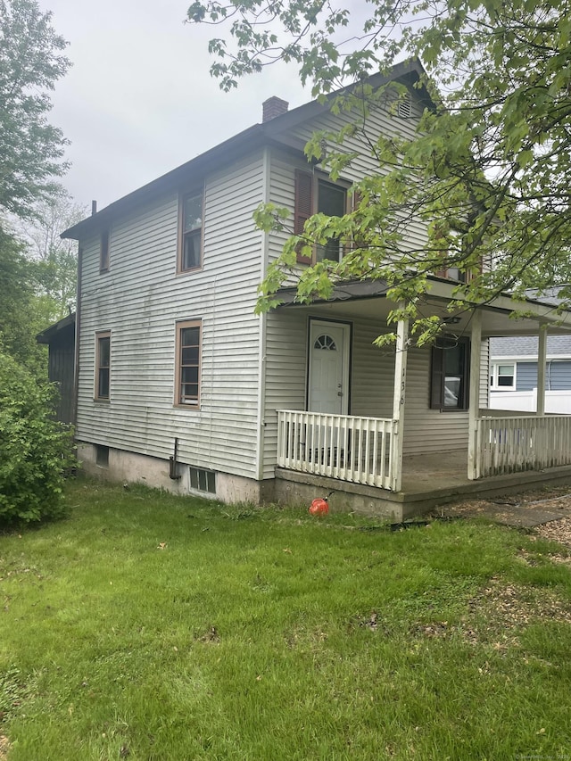 view of side of home featuring covered porch, a lawn, and a chimney