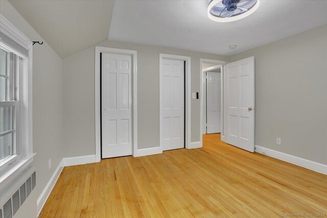 184 Goodale Dr, Newington, CT 06111 - unfurnished bedroom with baseboards, radiator, light wood finished floors, two closets, and lofted ceiling