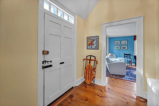 foyer entrance with hardwood / wood-style floors, vaulted ceiling, and baseboards