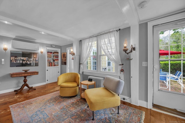 sitting room featuring radiator, a wall unit AC, hardwood / wood-style flooring, and baseboards