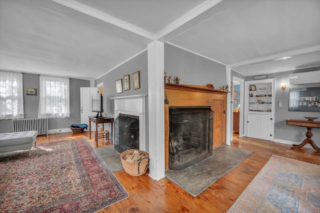 living room with a fireplace with flush hearth, radiator, hardwood / wood-style flooring, a wall unit AC, and ornamental molding