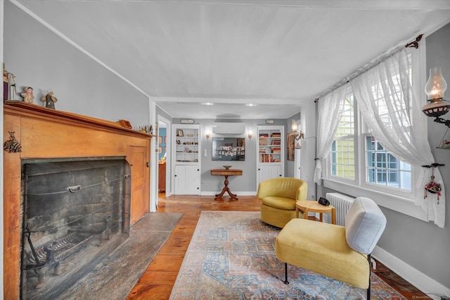 living area with a wall mounted air conditioner, radiator, a fireplace with flush hearth, hardwood / wood-style floors, and built in shelves