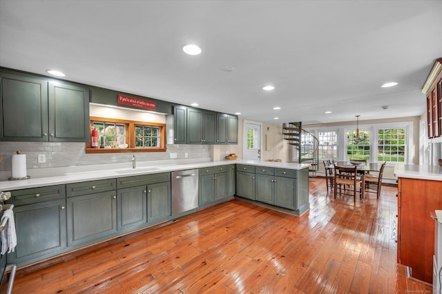 kitchen with stainless steel dishwasher, green cabinetry, a peninsula, a sink, and plenty of natural light