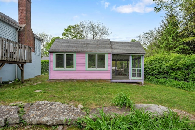 rear view of house with a sunroom, a yard, and roof with shingles