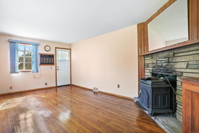 1 Cedar Rd, Danbury, CT 06811 - unfurnished living room featuring a wood stove, wood finished floors, a wall mounted AC, and baseboards