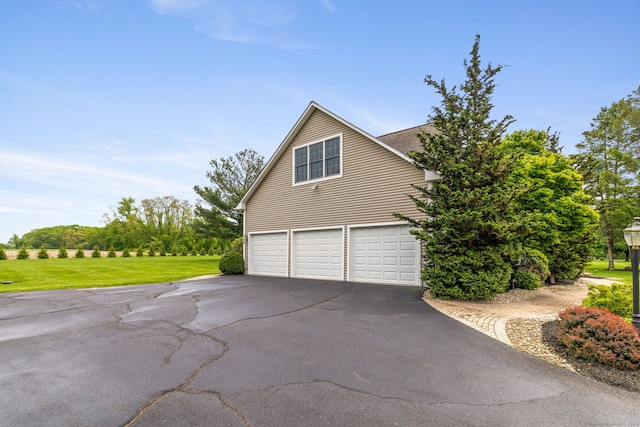 view of side of home featuring asphalt driveway, an attached garage, and a yard